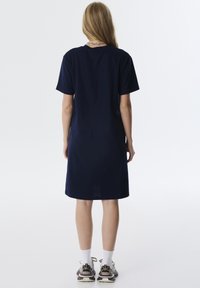 Navyblauw katoenen jurk met korte mouwen, losse pasvorm en jurk tot op de knieën. Gedragen met grijze en witte sport schoenen en sokken.