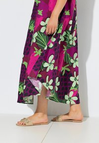 Maxiklänning med blommönster på en mörklila botten, med gröna och rosa blommor. Lätt, flödande tyg; beigea sandaler med platt sula och dekorationer.