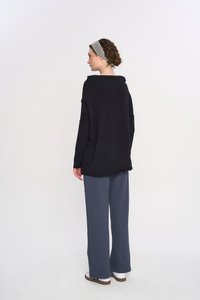 Przesadny czarny sweter z wysokim kołnierzem, długimi rękawami i luźnym krojem, zestawiony z luźnymi szarymi spodniami i białymi trampkami.