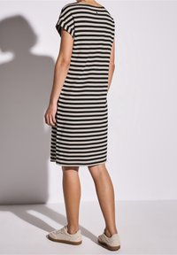 Czarna i beżowa sukienka w paski, krótki rękaw, długość do kolan, luźny krój, wykonana z miękkiego materiału, zestawiona z jasnymi butami.