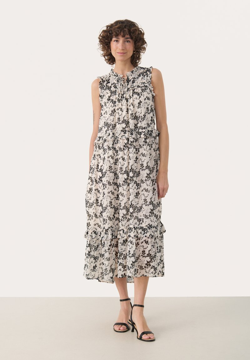 Rochie fără mâneci, cu imprimeu floral în crem și modele negre, cu detalii volan și design în straturi. Asortată cu sandale negre cu bretele.