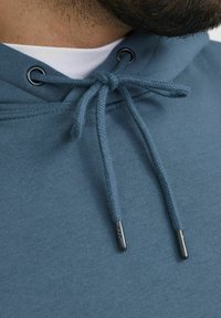 Hoodie in blauwe stof met een gladde textuur. Voorzien van een trekkoord met metalen aglets en een gelaagd wit shirt eronder.