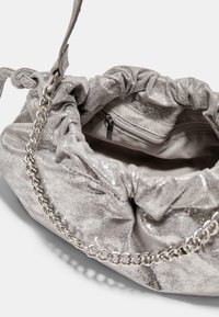 Sac métallique argenté avec un haut froncé, une bandoulière en chaîne et un intérieur lisse, doté d'une poche zippée pour un rangement sécurisé.