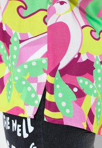 Farverig skjorte med et levende blomstret og abstrakt design i pink, grøn og gul. Lavet af letvægtsstof med en slidse i siden.