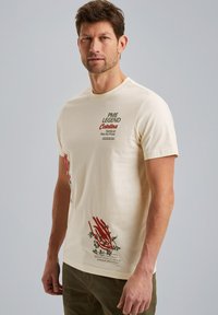T-shirt en coton crème avec des graphiques de plantes rouges et du texte sur le devant. Manches courtes, col ras du cou et coupe standard.