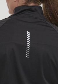 Svart idrottsjacka med hög krage, slät yta och ett vertikalt randmönster i vitt på baksidan.