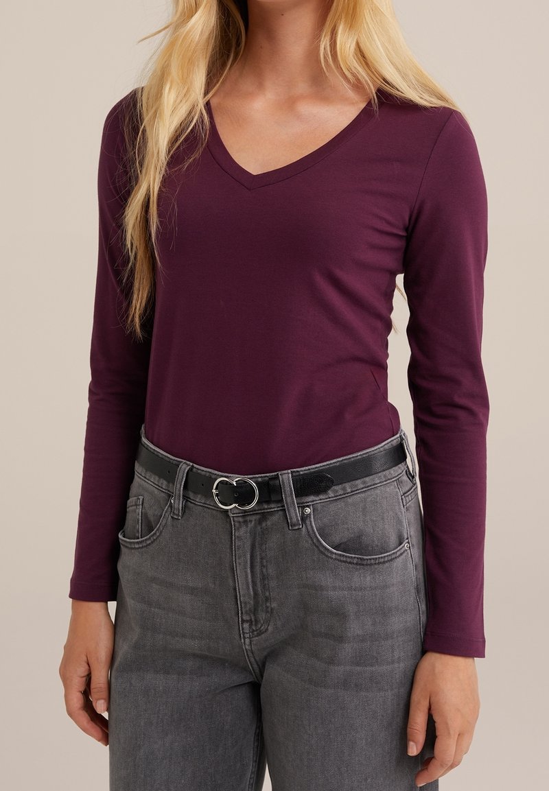 Maglietta a maniche lunghe con scollatura a V di un profondo bordeaux, abbinata a un paio di jeans grigi a vita alta e una cintura nera con una fibbia circolare argentata.