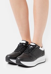 Black and white sneakers featuring a textured black upper with embossed detailing, flat black laces, and a white platform sole.