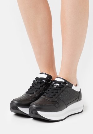 Schwarz-weiße Sneakers mit einem strukturierten schwarzen Obermaterial und erhabenen Details, flachen schwarzen Schnürsenkeln und einer weißen Plattformsohle.