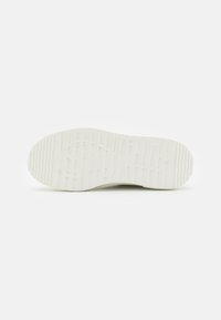 Fehér sneaker talp, textúrált tapadással, amely mintás felülettel és enyhe ívvel rendelkezik. Oldalán megjelenik a dombornyomott logo részlet.