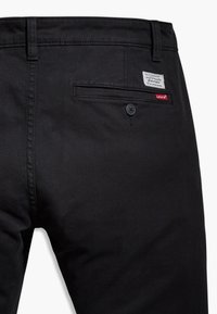 Black denim pants featuring a rear pocket, button closure, and a label patch with "Levi's" branding. Smooth texture and tailored fit.