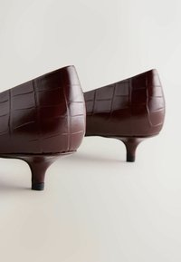 Brūnas lakādas augstpapēži ar krokodila faktūru, koniska forma un zema stiletto papēža. Melns papēža akcents pie pamatnes.