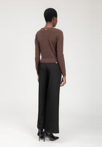 Brauner, taillierter Pullover mit langen Ärmeln und geripptem Saum, kombiniert mit schwarzen weit geschnittenen Hosen und schwarzen, höheren Stiefeletten.