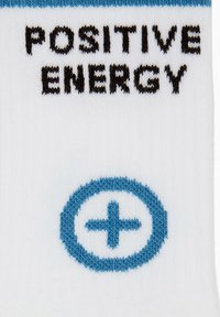Calzino bianco con scritta nera "POSITIVE ENERGY" sopra un cerchio blu con un segno più. Il design è lavorato a maglia con una texture liscia.