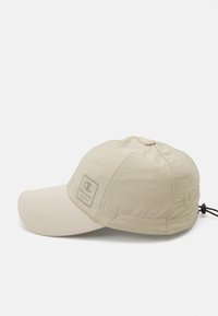 Beige baseball cap med glatt stoff, strukturert krone, flat skygge, og et logomerke på forsiden. Inkluderer justerbar krok bak.