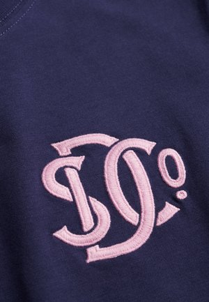 Marineblauwe katoenen stof met een roze geborduurd logo bestaande uit gebogen letters "D" en "O" met accenten en een punt.