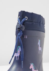 Marinblå gummistövlar för regn med rosa och lila enhörningsmönster, snörning i toppen med snörelock, slät yta och rund tå.