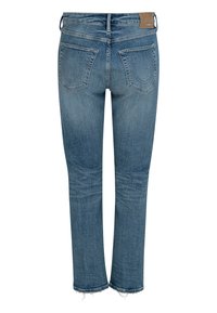 Niebieskie dżinsy z denimu z efektem wypłowienia, z pięcioma kieszeniami i postrzępionym wykończeniem na dole. Posiadają brązową skórzaną łatę z tyłu jako znak firmowy.