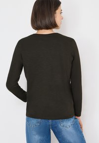 Dunkelgrünes Langarmshirt mit rundem Ausschnitt, glatter Textur und lässiger Passform, kombiniert mit hellblauen Jeans im klassischen Denim-Stil.