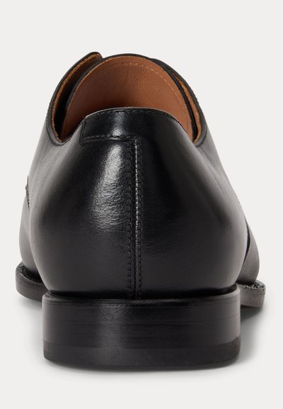 Black leather dress shoe viewed from the back, showing smooth texture, stitching, and brown interior lining.