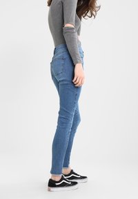 Úzké modré džíny vyrobené z denimu, s vysokým pasem, mírným třepením na lemu a přiléhavým střihem. V kombinaci s černými teniskami Vans.