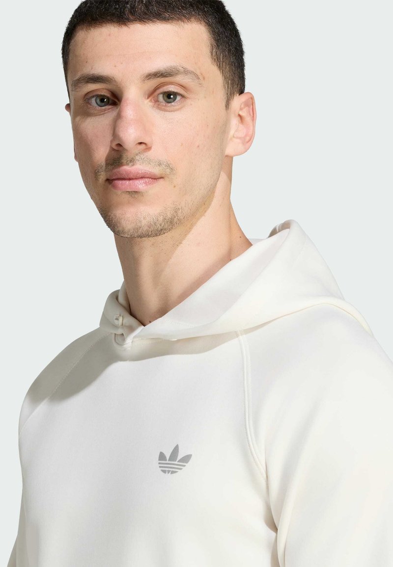 Man with short dark hair wearing a white Adidas hoodie with a small gray logo on the chest, facing forward with a neutral expression.