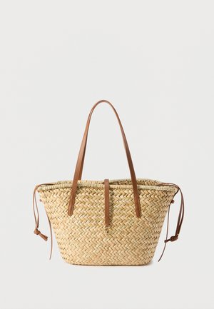 Πλεκτή τσάντα ώμου από ψάθα με μακριές καφέ δερμάτινες λαβές, δερμάτινο λουράκι με χρυσό κούμπωμα και πλαϊνά κορδόνια στήριξης σε ανοιχτό φόντο.