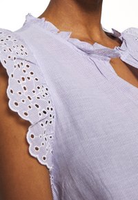 Vaaleanpunertava raidallinen yläosa, jossa on röyhelöinen pääntie ja pitsireunaiset hihat, joissa on pieniä leikkauksia reunoilla. Sileä kangaspinta.