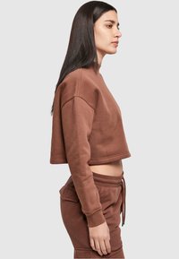 Bruine cropped sweatshirt met lange mouwen, gemaakt van zacht materiaal. Voorzien van een ronde halslijn en gecombineerd met bijpassende joggers.
