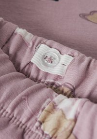 Elastična traka u struku ružičastih dječjih hlača s podesivim bijelim gumom iznutra, koja prikazuje slabo bež i bijeli uzorak.