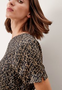 Blusa nera con un tessuto testurizzato, caratterizzata da un motivo geometrici beige e maniche a scallop. Primo piano del collo e della spalla.