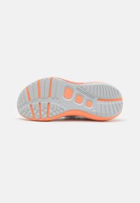 Semelle d'une basket Under Armour orange et grise avec motifs de grip texturés et logo de la marque au centre.