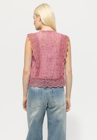 Spitzen-Top in zartem Rosa mit gewellten Kanten und einem detailreichen Muster, kombiniert mit blauen, weiten Denim-Jeans.