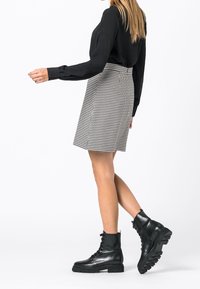 Svart skjorta med långa ärmar, rutig grå kjol och svarta snörkängor med en robust sula. Modern, strukturerad design.