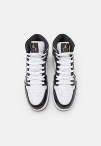 Vysoké tenisky s černým lakovaným povrchem a bílými koženými sekcemi, kulatou špičkou a bílými tkaničkami. Zlatý detail loga na jazyku.