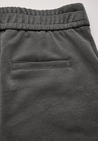 Le pantalon de jogging gris présente une texture lisse, une taille élastique et une seule poche arrière avec des coutures soignées.