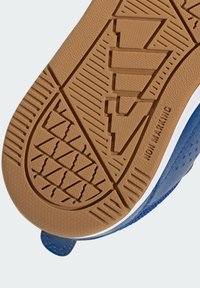 Podeszwa buta wykonana z teksturowanej gumy w kolorze beżowym, z geometrycznymi wzorami bieżnika oraz niebieskim syntetycznym brzegiem cholewki. Obecna jest etykieta informująca o niepozostawianiu śladów.