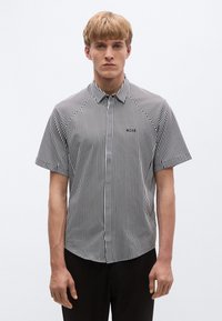 Cămașă cu nasturi cu mâneci scurte, în dungi alb-negru, cu guler, broderie pe piept și croială ajustată.