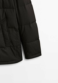 Giacca a vento nera con design trapuntato, dotata di una tasca con zip sul lato e una texture liscia. Maniche lunghe e imbottite per il calore.