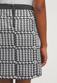 Falda de pata de gallo en blanco y negro con tejido texturizado, que cuenta con una cremallera visible en la parte posterior y una cinturilla elástica gruesa.