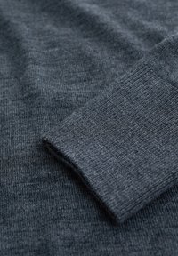 Manche de pull en maille gris foncé montrant un poignet côtelé et une texture lisse, avec des détails en gros plan du tissage du tissu et des coutures.