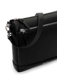 Czarna skórzana torba o fakturowanej powierzchni, z zamkiem błyskawicznym u góry, regulowanym paskiem na ramię oraz srebrnymi elementami wykończenia.