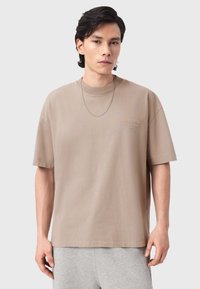 Μπεζ κοντομάνικο μπλουζάκι από απαλό βαμβάκι με άνετη γραμμή, διαθέτοντας ένα διακριτικό ανάγλυφο λογότυπο στο στήθος και λαιμόκοψη τύπου μπλούζας.