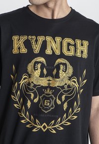 Camiseta de algodón negra con diseño impreso en dorado que incluye el texto "KVNGH", dos fénixes, una corona y un motivo de laurel.