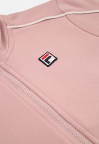 Rosa zip-up sweatshirt med ribbad krage, med en broderad logga i röd, blå och vit på vänster bröst. Mjuk tygkänsla.
