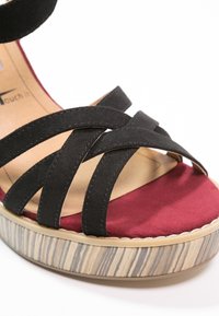 Sandale en suède noir à brides croisées, semelle intérieure bourgogne et plateforme à texture bois.
