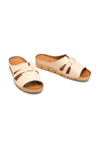 Beżowe skórzane klapki z otwartymi palcami, z wyciętymi wzorami i drewnianą platformą o teksturowanych krawędziach.