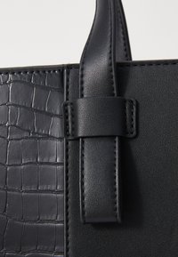 Sac à main noir avec une surface texturée en croco embossé et des accents en cuir lisse. Les poignées sont maintenues par une boucle rectangulaire.