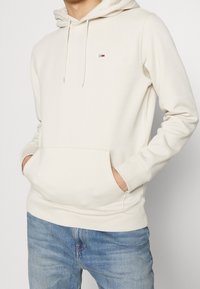 Felpa di colore crema realizzata in misto cotone, con tasca anteriore, cappuccio con cordini e piccolo logo sul petto. Vestibilità casual con polsini a coste.