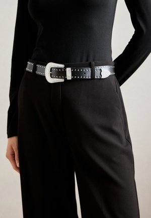 Cintura in pelle nera con una grande fibbia argentata decorata con strass e borchie metalliche lungo la cinghia per un tocco di dettaglio in più.